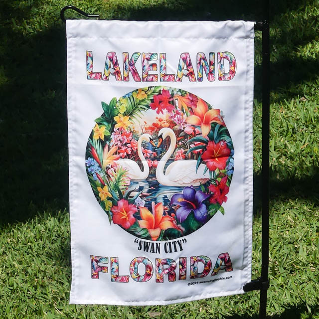 Floral Swan City Flag, LAKELAND top, FLORIDA bottom, colorful circular floral motif, lifestyle pic hanging on wire stand in garden